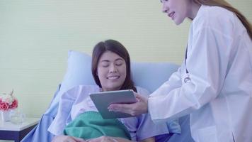 Beautiful smart Asian doctor and patient discussing and explaining something with tablet in doctor hands. video