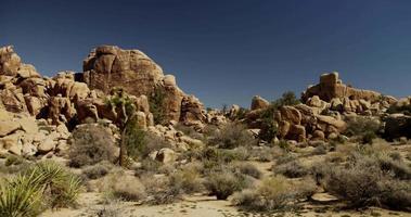 Schwenkaufnahme des kleinen Felsenhügels in der Wüstenlandschaft mit stacheligen Pflanzen im Vordergrund in 4k video