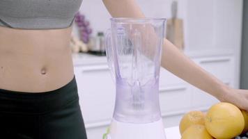 Sporty Asian woman using blender to make grape juice in the kitchen. video