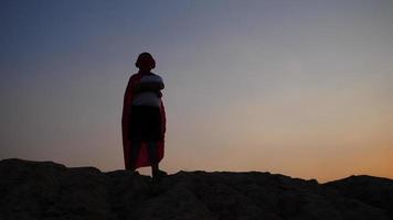 Silhouette eines Jungen, der Spaß hat, der als Superheld verkleidet ist, der in einem Feld läuft video