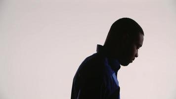 Silhouette of a young black man tilting his head down and then turning to the right of the scene thinking worried video