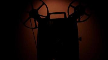 vista laterale di una silhouette di un proiettore cinematografico da 8 mm con bobine che girano con luce soffusa su sfondo in 4K video