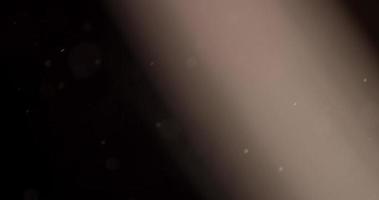 ljusa partiklar som korsar scenen från vänster till höger på mörk bakgrund med ljusstråle i 4k video