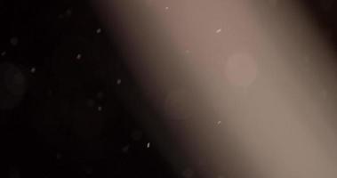 Soft particles going up on dark background with diagonal raylight in 4K video