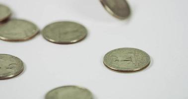  A lot of coins of quarter dollar falling and spinning over three coins on white table, seven coins placed in the scene in 4K video