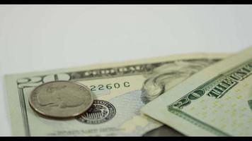 A lot of coins of quarter dollar falling over one coin and two $20 bills on white table, finally one coin and both bills placed in the scene in 4K video