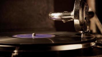 Dark scene of static medium shot of record player with vinyl disc illuminated from left side creating hards shadows in 4K video