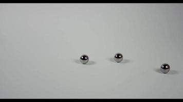 A big group of little metal balls falling and bouncing on white table in 4K video