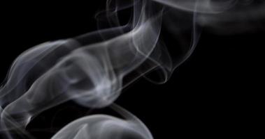 Soft controlled smoke in studio floating and drawing spirals, swirls and waves in darkness in 4K video