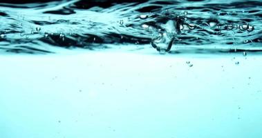 Blue scene of water container showing in upper section the water surface with waves and bubbles in thr right side in 4K video