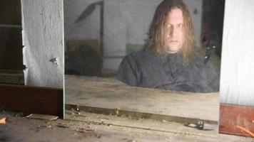 Depressed and angry man is sitting in front of his reflection in an old abandoned house video