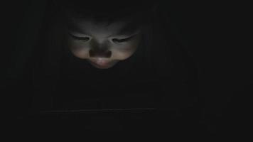 asiatischer kleiner Junge, der Tablet oder Smartphone auf einem Bett in der Nacht spielt video