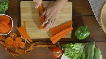 vista superior do chefe da mulher fazendo salada de alimentos saudáveis e picar cenoura em uma tábua na cozinha. video