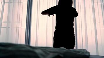 bella donna asiatica sveglia e in piedi vicino alla finestra mentre si allunga vicino al letto. video
