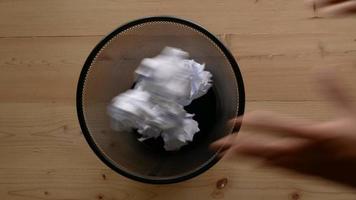 mão jogar papel amassado no lixo com fundo de mesa de madeira video