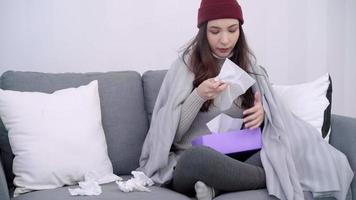 sjuk ung asiatisk kvinna känner huvudvärk som sitter på en stol insvept i grå filt i hennes vardagsrum hemma. video