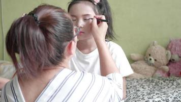 familia asiática con madre maquillando a su niña en la habitación. video