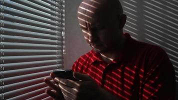 Man in red t-shirt scrolling through information on mobile phone in an office video