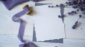 White blank card, envelope and ribbon on a background of pink and blue fabric with lavender flowers on a white background. video