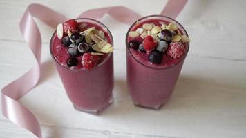 dois copos de milkshake de smoothies de frutas rosa ou smoothie ou coquetel em um fundo branco de madeira. video