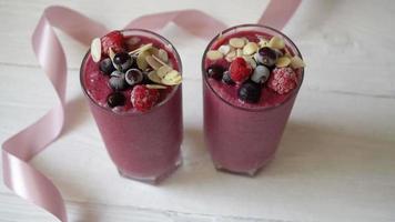 Dos vasos de batidos de frutas rosadas batido o batido o cóctel sobre un fondo de madera blanca. video