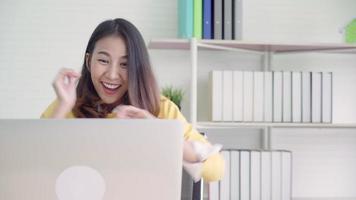 bella giovane donna asiatica sorridente in arrivo laptop sulla scrivania in soggiorno a casa. video