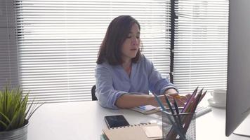 mooie jonge glimlachende Aziatische vrouw die op laptop komt zittend in een huiskamer. video