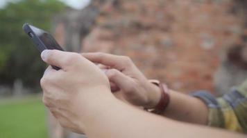 Voyageur homme asiatique à l'aide de smartphone vérifiant les médias sociaux tout en vous relaxant après avoir passé des vacances à Ayutthaya, Thaïlande video