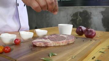 Cerca del chef gourmet o cocinera condimentando trozos frescos de carne de res con sal marina y pimientos picantes molidos. video