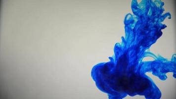 blaue Farbe Farbtinte strömt über das Glas mit fallenden Tintenbonbons und abstrakter Rauchexplosion.