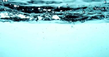 Blue scene of water splashing in big container generating bubbles in 4K video