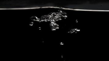 Shiny bubbles floating from lower section and exploding in the surface with dark background in 4K video