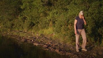 vecchia signora che cammina vicino a un lago con alberi sullo sfondo video