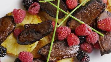 Rotating shot of a delicious smoked duck bacon dish with grilled pineapple, raspberries, blackberries, and honey - FOOD 093