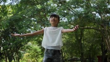Asian little girl playing outdoor in slow motion, Spinning and smiling and raising hands in the air 