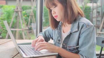 zakelijke freelance Aziatische vrouw komt, doet projecten op laptop en gebruikt smartphone zittend op tafel in café.