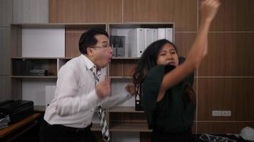 Two joyful colleagues in formal suits dancing cheerful in office video
