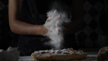 Ralenti des mains d'une femme tamisant la farine sur une pizza