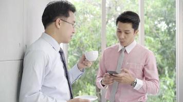 Slow motion - Young smiling men enjoying drinking warm coffee standing while relax in office. video