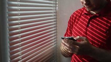 El hombre se para cerca de la ventana en la habitación del hotel y usa un teléfono inteligente. video