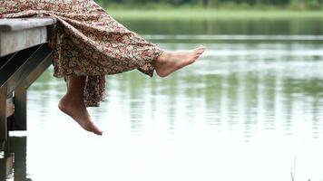 Frau, die ihre Füße am See schwingt, der am Rand eines hölzernen Docks sitzt video