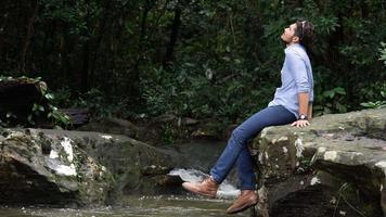 Hombre que viaja balanceando su pierna mientras se relaja junto al arroyo. video