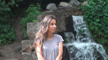 Young Woman Posing With A Waterfall As A Background.