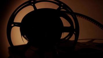 Silhouette of arrangement of three old film reels spinning to the right with warm illumination on background in 4K video