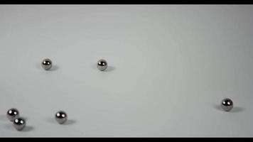 A lot of little metal balls falling and bouncing in three groups on white surface in 4K video