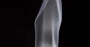 Thin column of white smoke spinning in vertical axis on black background in 4K video