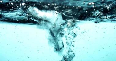 Escena azul de agua salpicando de izquierda a derecha, generando ondas y burbujas en 4k video