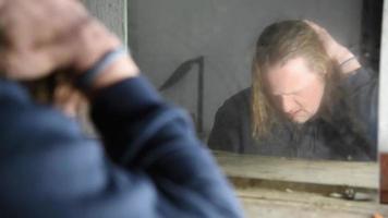 homem deprimido e zangado está sentado em frente a seu reflexo em uma velha casa abandonada