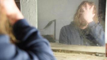 Depressed and angry man is sitting in front of his reflection in an old abandoned house video