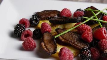 Rotating shot of a delicious smoked duck bacon dish with grilled pineapple, raspberries, blackberries, and honey - FOOD 115 video